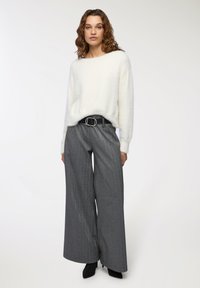 Pullover bianco soffice con scollo ampio, abbinato a pantaloni grigi a vita alta con gamba larga, accentuati da una cintura nera con fibbia argentata.