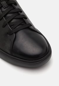 Adidași din piele neagră, cu vârf rotund, șireturi texturate, suprafață netedă și talpă din cauciuc cu un ușor detaliu de profil.