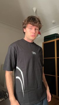 T-shirt preta de mangas curtas com gola redonda, apresentando um elemento de design branco no lado esquerdo e um pequeno logótipo no peito.