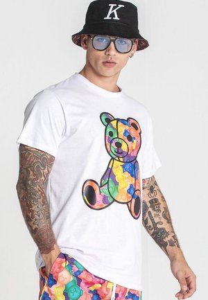 Camiseta blanca con un gráfico colorido de osito de goma. El diseño incluye colores vibrantes y se combina con pantalones cortos estampados.