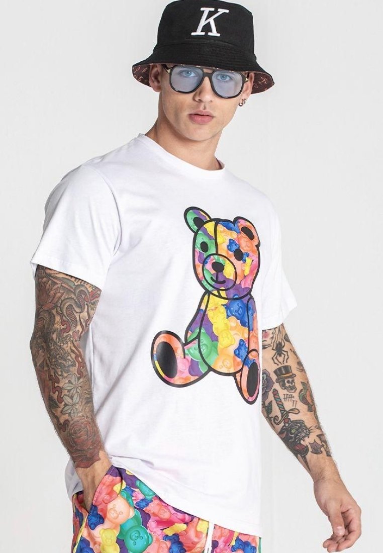 Camiseta blanca con un gráfico colorido de osito de goma. El diseño incluye colores vibrantes y se combina con pantalones cortos estampados.