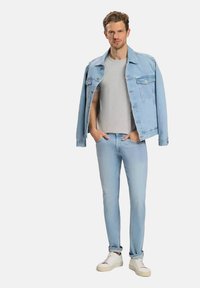 Jasnoniebieska kurtka dżinsowa z szarym t-shirtem, jasnoniebieskimi dżinsami i białymi trampkami. Kurtka ma dwie przednie kieszenie i luźny krój.