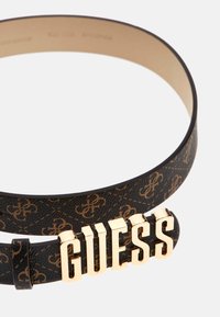 Cintura in finta pelle nera con un delicato motivo a rilievo e una spiccata fibbia con logo "GUESS" in tono oro. Texture liscia e vestibilità regolabile.