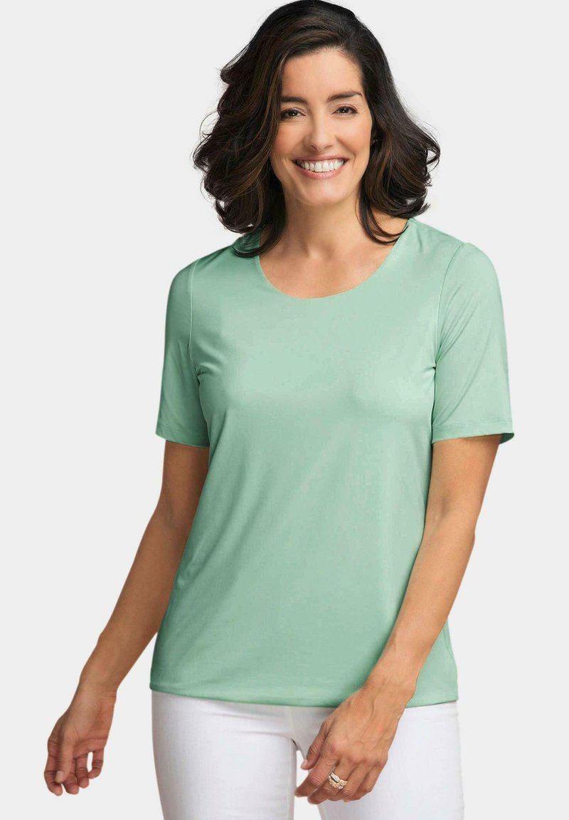 T-shirt à manches courtes de couleur menthe avec un col rond et une texture lisse, associé à un pantalon blanc.