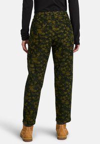 Groene broek met bloemendessin van textuurstof, met een rechte snit, achterzakken en omgeslagen enkels, gecombineerd met bruine schoenen.