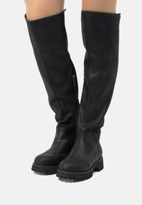 Botas negras hasta la rodilla hechas de cuero suave, con una suela gruesa, cremallera lateral y un diseño ligeramente caído.