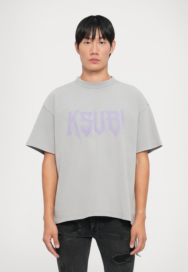 Grå oversized t-skjorte laget av myk stoff, med en lilla "KSUBI"-trykk over brystet. Korte ermer og et avslappet halsdesign.