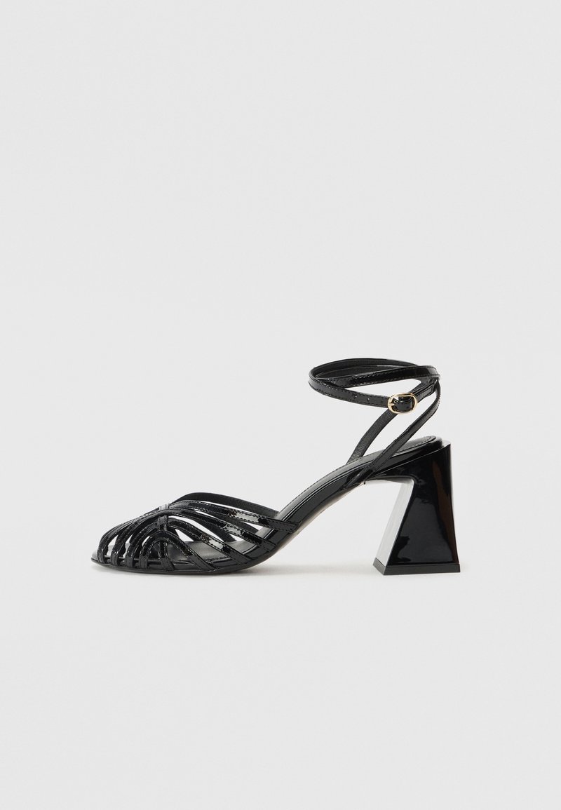 Sandales à talons noires à lanières avec un design tissé, un talon carré épais, et une bride de cheville avec une boucle dorée.