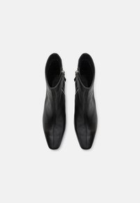 Botine negre din piele cu vârf ascuțit, siluetă subțire și fermoare laterale, având o textură netedă și un design minimalist.