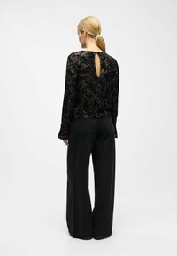 Black sequined top with long sleeves and a back keyhole detail, paired with black wide-leg pants. Fabric appears textured and reflective.