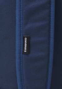 Bolso textil azul marino con una etiqueta negra de Converse, con costuras visibles y una superficie suave y duradera.