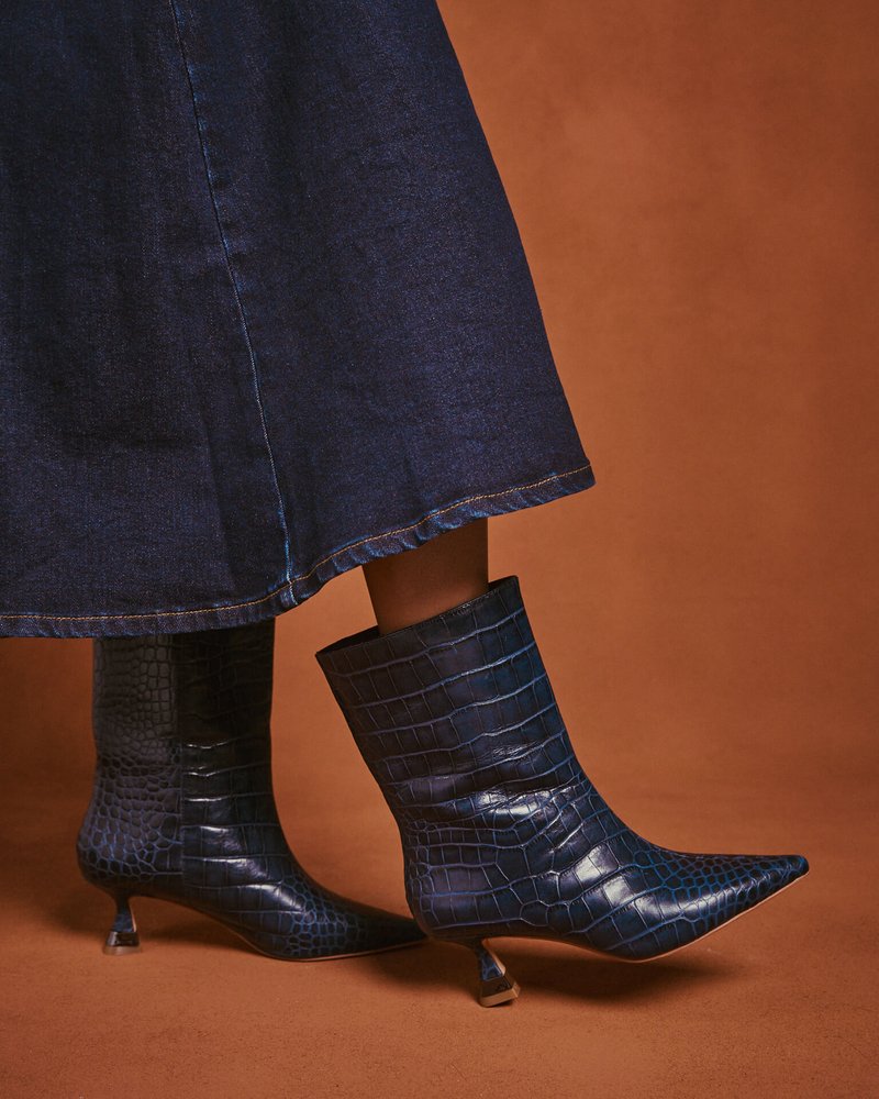 Botas de tobillo azul marino con estampado de cocodrilo, con puntera afilada y tacones en forma de cono, que presentan un acabado brillante y un diseño estructurado.