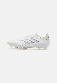 Weißer Fußballschuh mit blauen Akzenten, schlankem Design, strukturiertem Obermaterial und transparenten Stollen für Halt auf Rasenflächen.