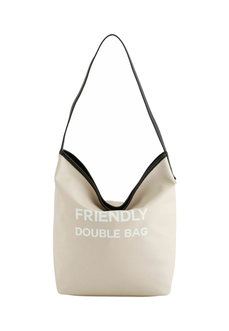 Beige hobo taske lavet af tekstureret materiale med en sort accent, der har teksten "FRIENDLY DOUBLE BAG" i hvid. Blød, slasket design.