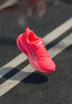 Zapatilla de running de color rosa brillante con el logo de Nike en gris, elevada sobre una carretera asfaltada con una raya blanca.