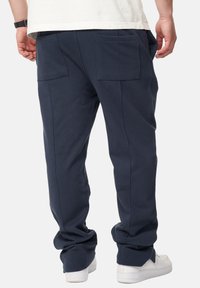 Marineblaue Sweatpants mit lässigem Schnitt, ausgestattet mit zwei Gesäßtaschen und schmal zulaufenden Beinen, aus weichem Stoff, kombiniert mit weißen Sneakers.