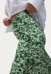 Jupe à motifs verts et noirs en tissu extensible, dotée d'une taille haute et d'un design ajusté. Des accents blancs créent un effet tacheté.