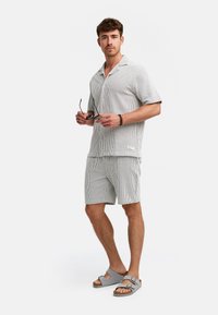 Kortærmet skjorte og shorts sæt i hvid med sorte lodrette striber. Båret med grå sandaler. Accessories inkluderer solbriller og et armbånd.