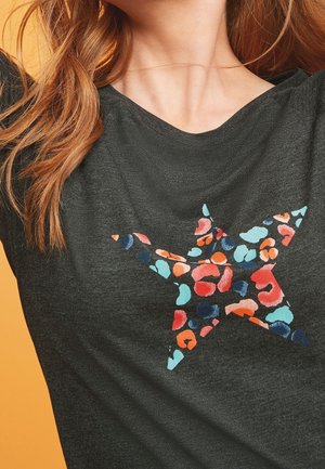 T-shirt gris foncé avec un design graphique étoilé coloré, présentant des motifs abstraits rouges, bleus et oranges sur un tissu texturé.