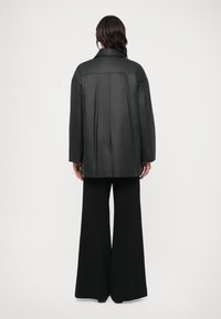 Casaco oversized preto feito de tecido suave com colarinho tipo notched. Combinado com calças largas pretas. Detalhes de costura na parte de trás.