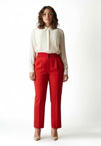 Weiße Bluse mit langen Ärmeln und Kragen, kombiniert mit hoch taillierten roten Hosen. Strukturierte goldene Absätze vervollständigen den Look.