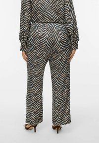 Wide-leg pants feature a zebra-stripe pattern in brown and black on a smooth fabric, with an elastic waistband and discreet pockets.