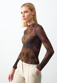 Langsleeve, geribbelde top in bruine en oranje tinten, met een hoge hals en een getailleerde pasvorm, gecombineerd met lichtgekleurde, geplisseerde broeken.