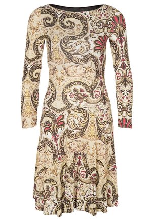 Femme portant une robe longueur genou à manches longues avec un motif floral orné beige, noir et rouge, des collants noirs transparents et des talons noirs.