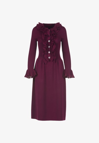 Megzta suknelė tamsiai burgundiško atspalvio, su ilgomis rankovėmis, raukšlėtu apykakliu, mygtukų užsegimu priekyje ir išplatintais raukšlėtais rankogaliais. Lygus paviršius ir prigludusi liemens linija.