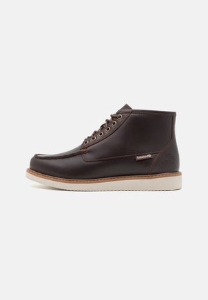 Stivale alla caviglia in pelle marrone con punta arrotondata, sole beige, occhielli in ottone, lacci marroni e logo Timberland sul lato.