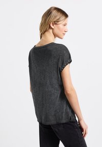 T-shirt à manches courtes gris foncé avec une coupe décontractée, présentant un ourlet à motifs le long des manches et un col arrondi. Texture douce.