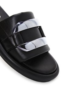 Sandale mule en cuir noir avec une large bride et deux accents métalliques argentés brillants sur le dessus.