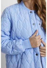 Vaaleansininen tikattu bomber-takki timanttikuvioidulla ompelulla, nepparikiinnityksellä ja resorikääreillä hihoissa. Sileä kangaspinta ja kapean leikkauksen design.