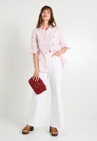 Chemise à rayures roses avec des accents brodés, assortie à un pantalon large blanc. Accessoirisée avec une pochette rouge et des sandales à plateforme marron.