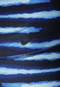 Niebieska materiał sportowy w wzory z ciemnoniebieskimi i jasnoniebieskimi poziomymi paskami. Logo Nike w czerni, z kontrastowym ściem na szwach.