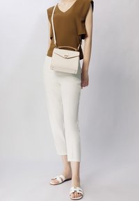 Brązowy top w serek, białe dopasowane spodnie, białe sandały z paskiem oraz mała torebka w kolorze kremowym z fakturą i złotym akcentem.