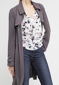 Długi szary płaszcz na kwiatowy top, połączony z ciemnoniebieskimi dżinsami. Płaszcz ma szeroki kołnierz i podwinięte rękawy.