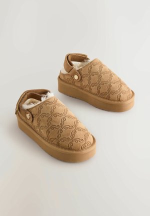 Hnedé semišové slip-on topánky s textúrovaným vzorom, mäkkou podšívkou a gumovou podrážkou. Majú bočný prackový detail a otvorený zadný dizajn.