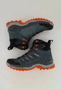 Scarpe da trekking con tomaia grigio-blu, supporto alla caviglia nero, dettagli arancioni e suola arancione robusta. Presentano lacci e strisce di ventilazione.