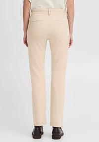 Beiga slim-fit byxor i ett mjukt tyg, med bakfickor och skräddarsydd midja, tillsammans med svarta skor.