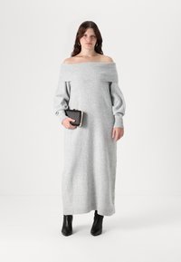 Siva pletena obleka brez naramnic z rebrastim ovratnikom in voluminoznimi rokavi. Kombinirana z črno torbico in gležnjarji. Gladka tekstura.