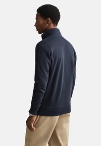 Marineblauwe sweatshirt met hoge kraag, gestructureerde stof, geribbelde manchetten en zoom. Gestyled met beige broek in een ontspannen pasvorm.