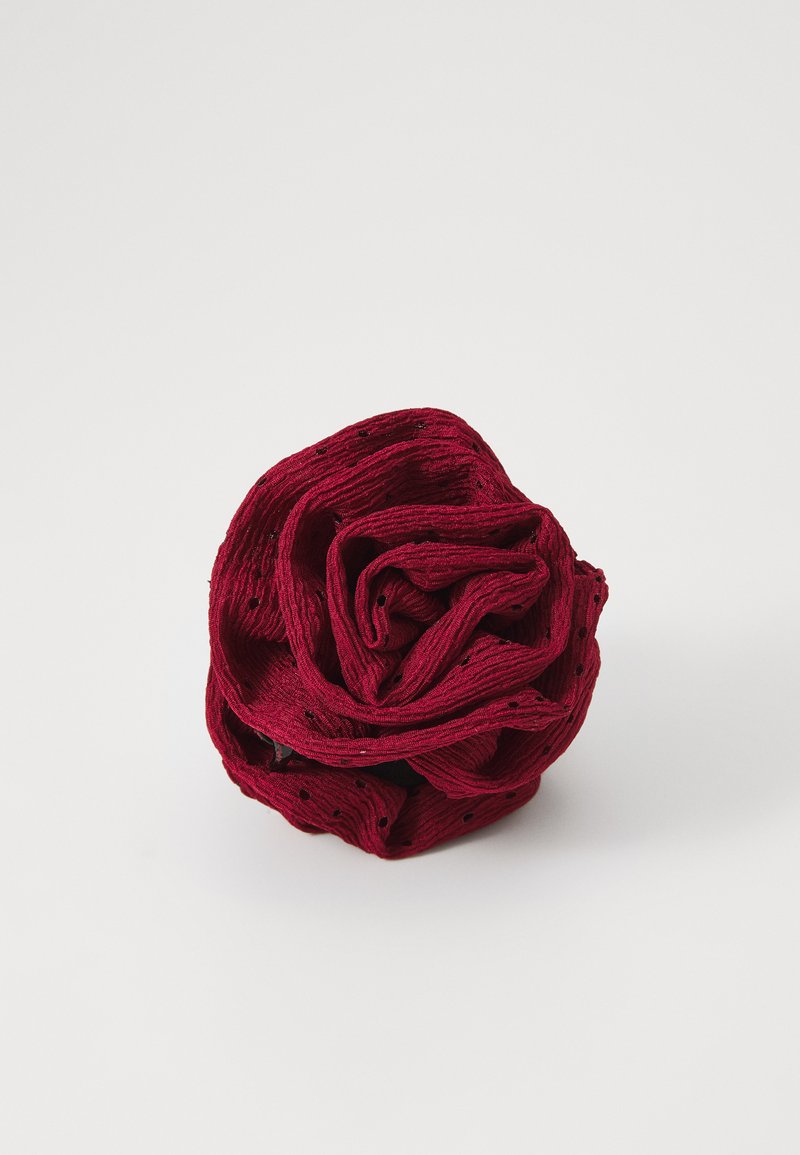 Rød stoffblomst med plisserte teksturer, laget av krøllet materiale. Har lagdelte kronblader og en svart base for stabilitet.