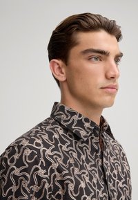 Camicia nera con un motivo a corda bianca, colletto abbottonato e bottoni neri, tessuto texturizzato e design aderente.