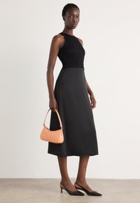 Abito nero senza maniche con corpino strutturato e gonna liscia, abbinato a una borsa arancione e scarpe con punta nera.
