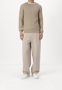 Beżowy prążkowany sweter z długimi rękawami, zestawiony z jasnobeżowymi spodniami o szerokich nogawkach i białymi sneakersami. Prosty, casualowy design.