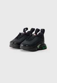 Ζευγάρι μαύρων αθλητικών παπουτσιών με υφαντά άνω τμήματα, με λωρίδες μαζέματος στην πτέρνα και πράσινες σόλες με αερόσολες, τοποθετημένο σε αχνό ελαφρύ φόντο.