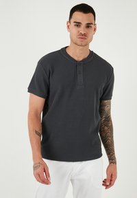Maglietta henley grigia scura a maniche corte con un tessuto texturizzato, caratterizzata da una fila di bottoni e un collo rotondo.