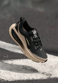 Baskets de course noires avec un dessus texturé, semelle intermédiaire crème et lignes d'accentuation noires. Comprend des lacets, un logo et une semelle rembourrée pour le soutien.