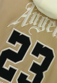 Beige stof met witte "Angel"-letters en een groot zwarte "23" met witte contouren. Gestructureerde witte capuchon.